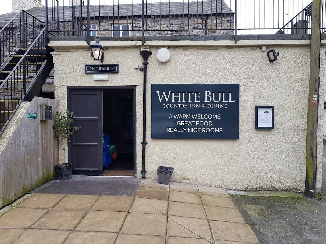 Entrance to The White Bull pub, featuring a sign with welcoming messages, stone walls, and a staircase in the background.