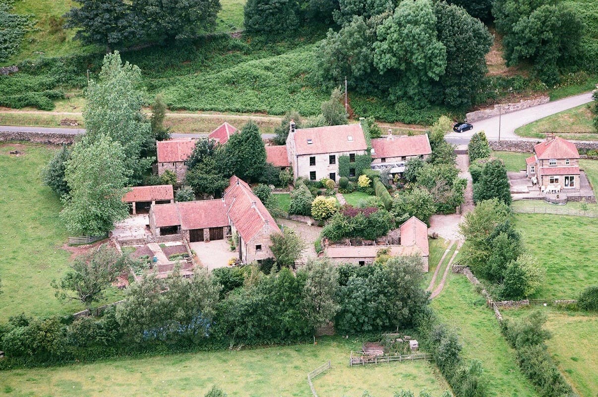 Aerial view of Red House Farm featuring several buildings, lush greenery, and a winding road in Glaisdale, Yorkshire.