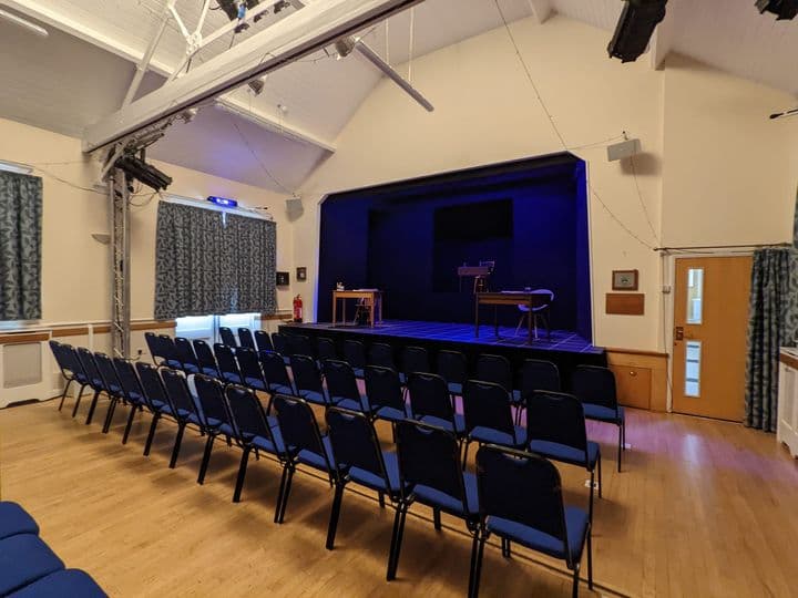 Interior of Robinson Institute Village Hall with rows of blue chairs facing a stage and blue lighting.