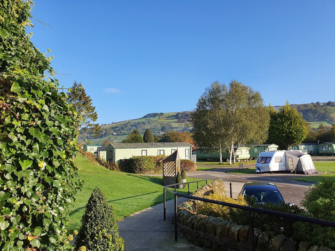 Caravans nestled among greenery with rolling hills in the background under a clear blue sky at Riverside Caravan Park.