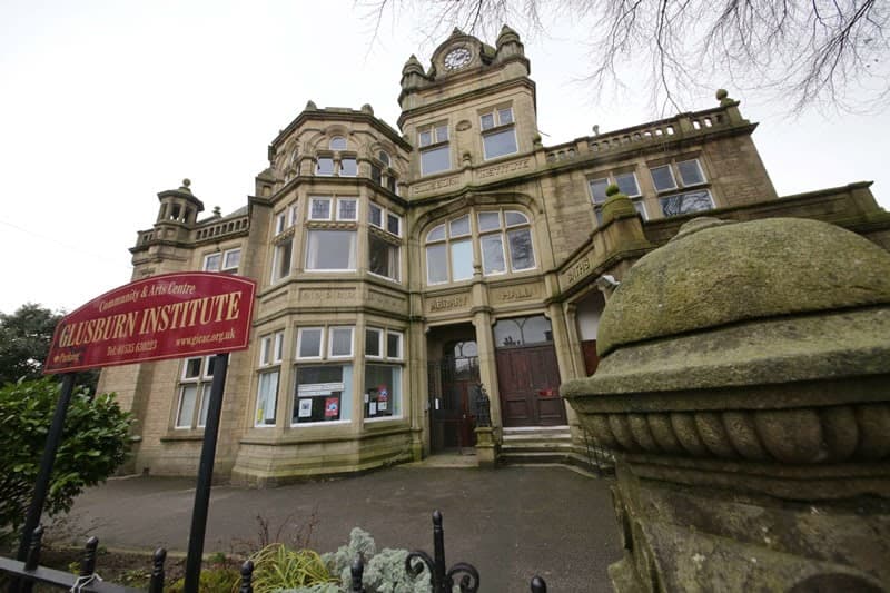 Victorian-style building with ornate stonework and a clock tower, featuring a sign for Glusburn Institute.