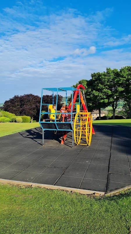 Colorful playground equipment with swings and slides on a grassy area under a blue sky with scattered clouds.