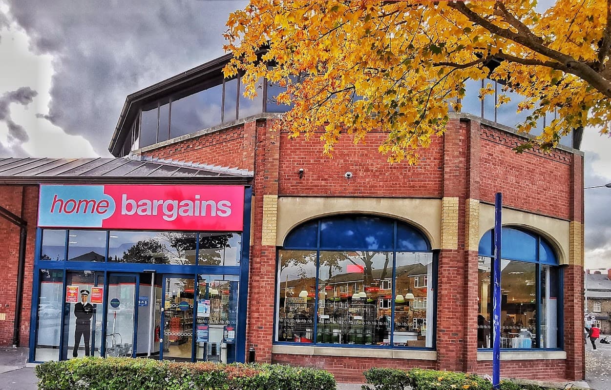 Red brick shop front with large windows, "home bargains" sign, and autumn leaves in the foreground.