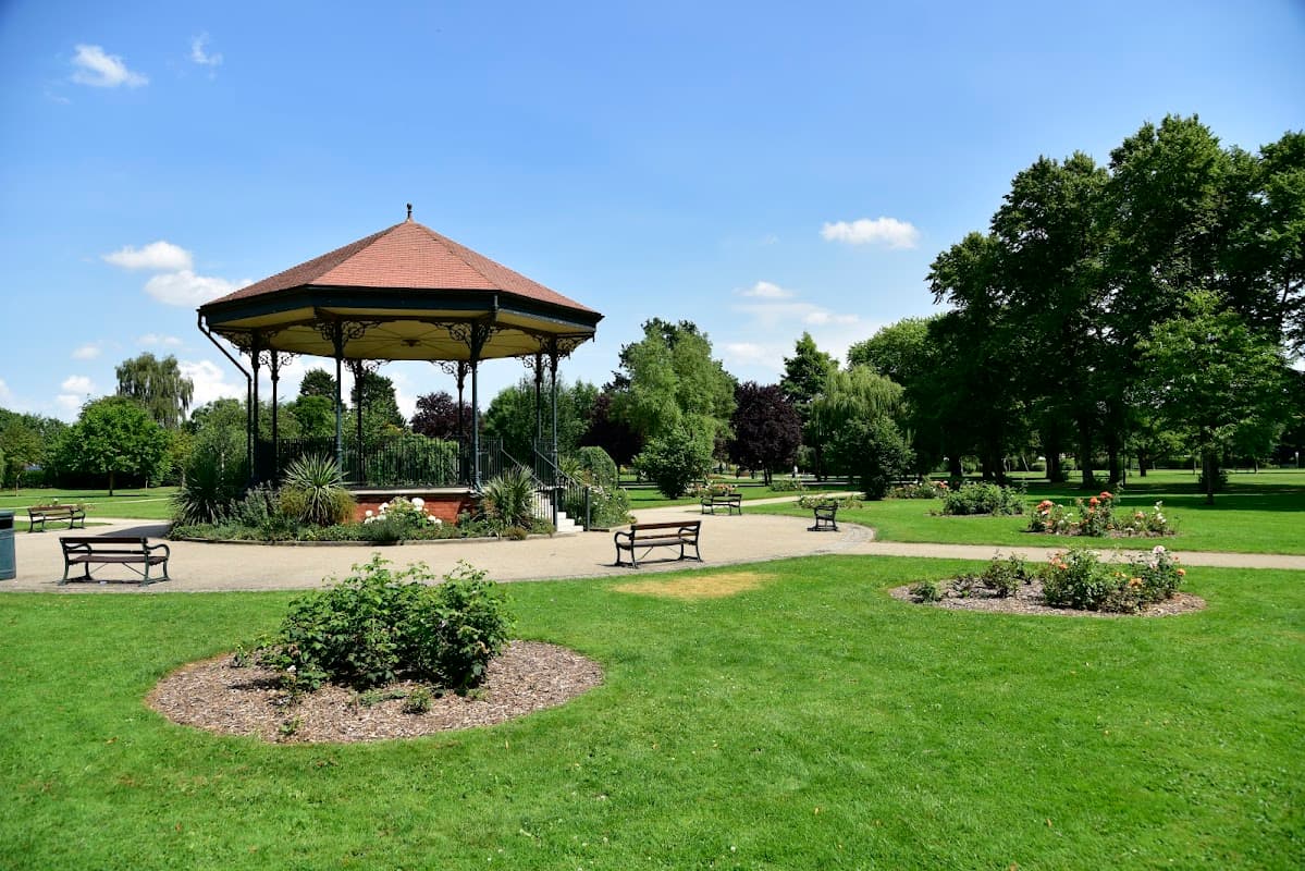 Victorian-style bandstand surrounded by well-maintained gardens and benches in a sunny park setting.