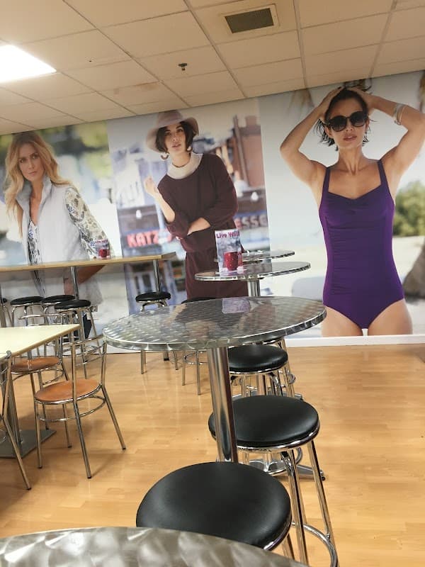 Fashion store interior featuring large wall displays of models in stylish outfits and a seating area with metal tables and stools.