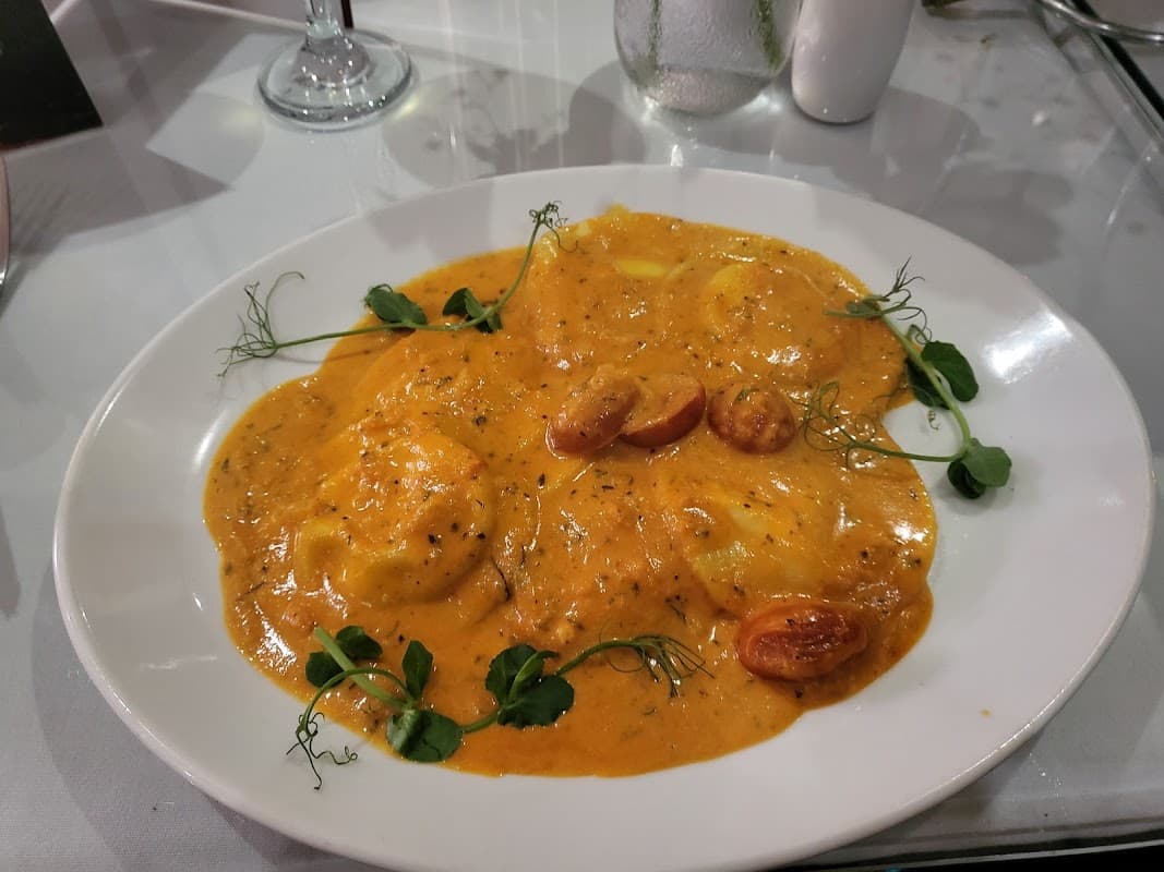 Plate of ravioli in a creamy tomato sauce, garnished with herbs and cherry tomatoes, on a white tablecloth.