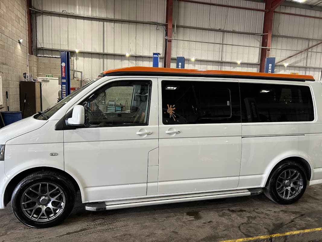 White van with an orange roof, sleek wheels, parked inside a spacious workshop with tools and equipment visible.