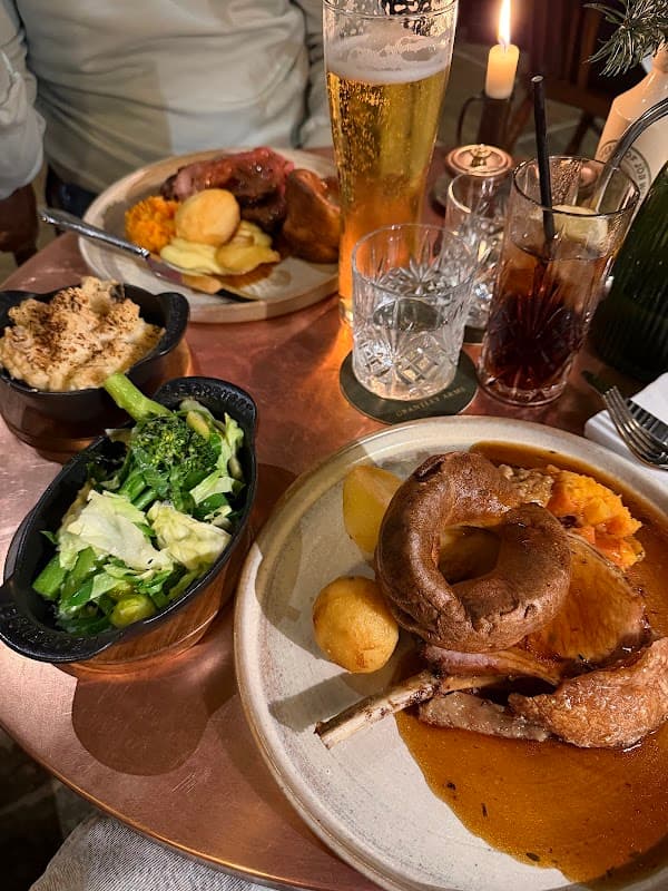 A table setting with plates of roast dinner, vegetables, a pint of beer, and a glass of dark drink.