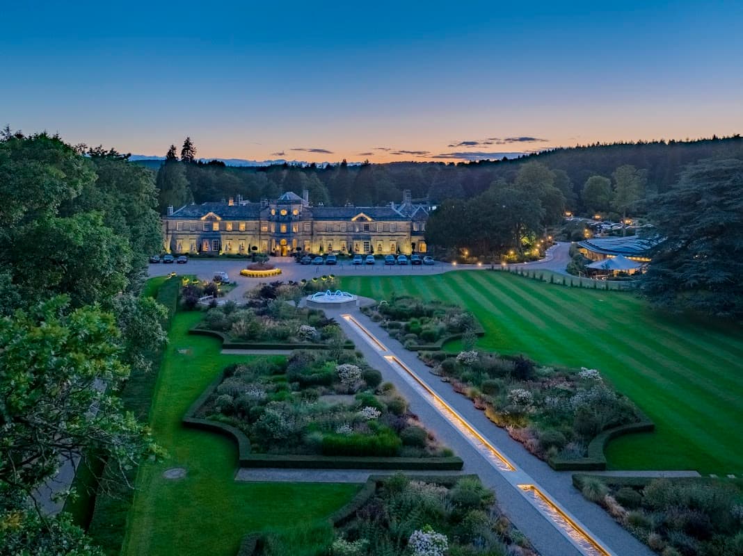 Elegant event venue at dusk, featuring manicured gardens, a fountain, and a grand building surrounded by trees.