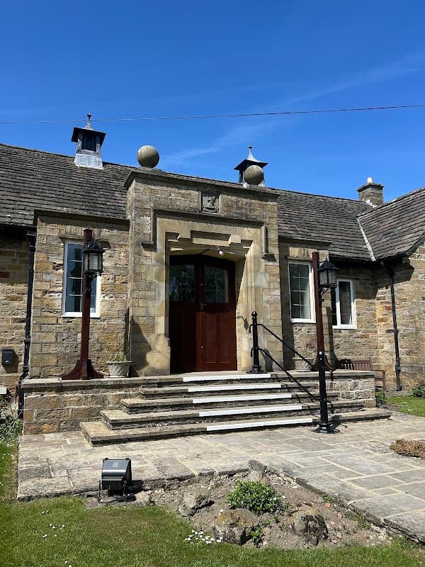 Stone entrance with steps, decorative lanterns, and a clear blue sky above Grantley Village Hall in Yorkshire.