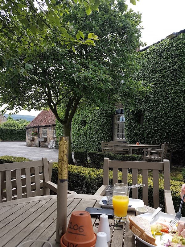 Outdoor dining area with wooden tables, lush greenery, and a view of a stone building in Great Broughton.