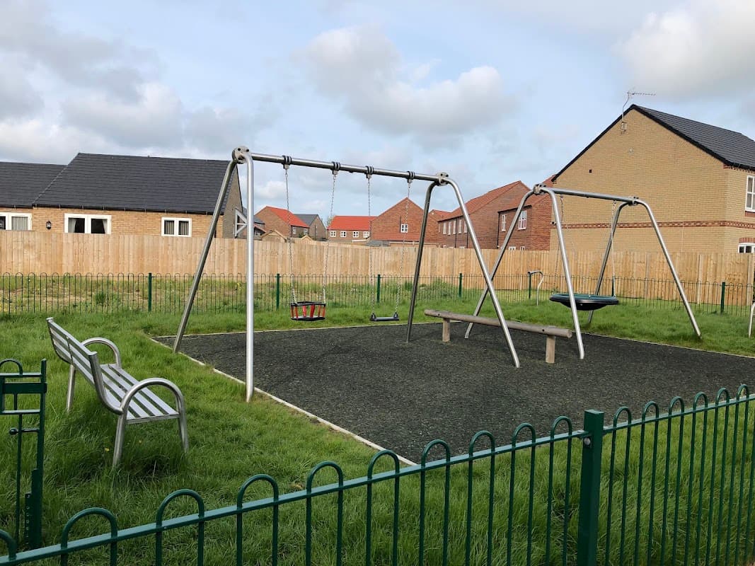 Play area with swings and a bench, surrounded by grass and residential houses in Great Driffield, Yorkshire.