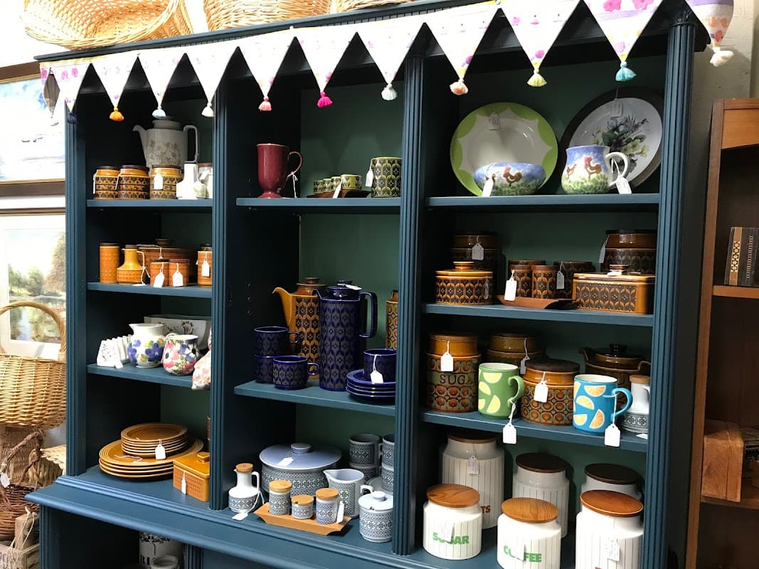 Colorful kitchenware displayed on shelves, including teapots, mugs, and jars, with decorative bunting above.