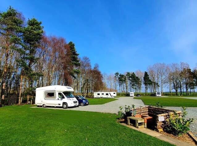 Campsite with caravans and motorhomes, surrounded by trees and a clear blue sky in Great Hatfield, Yorkshire.