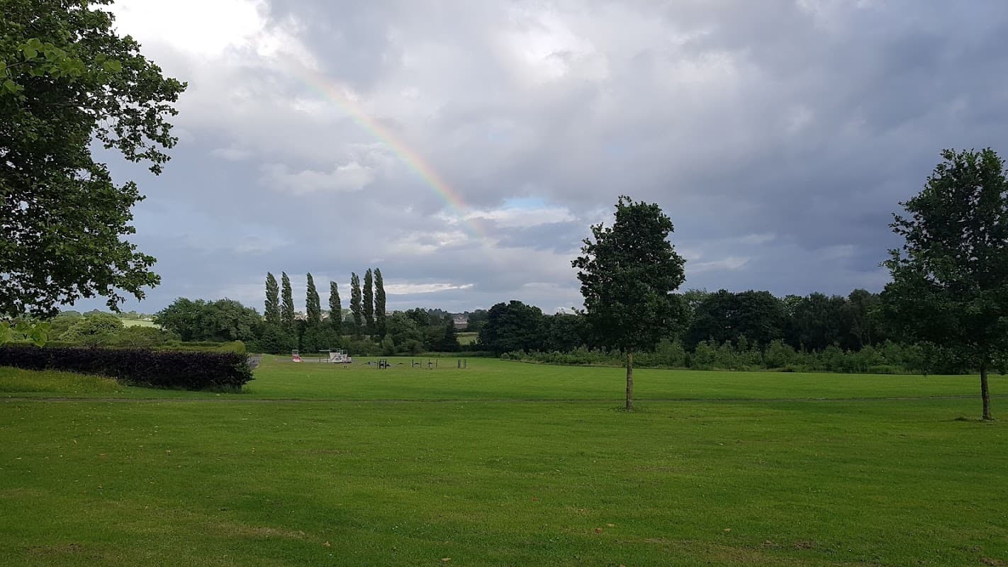 Lush green park with trees, a rainbow in the cloudy sky, and open grassy areas in Greenhill, Yorkshire.
