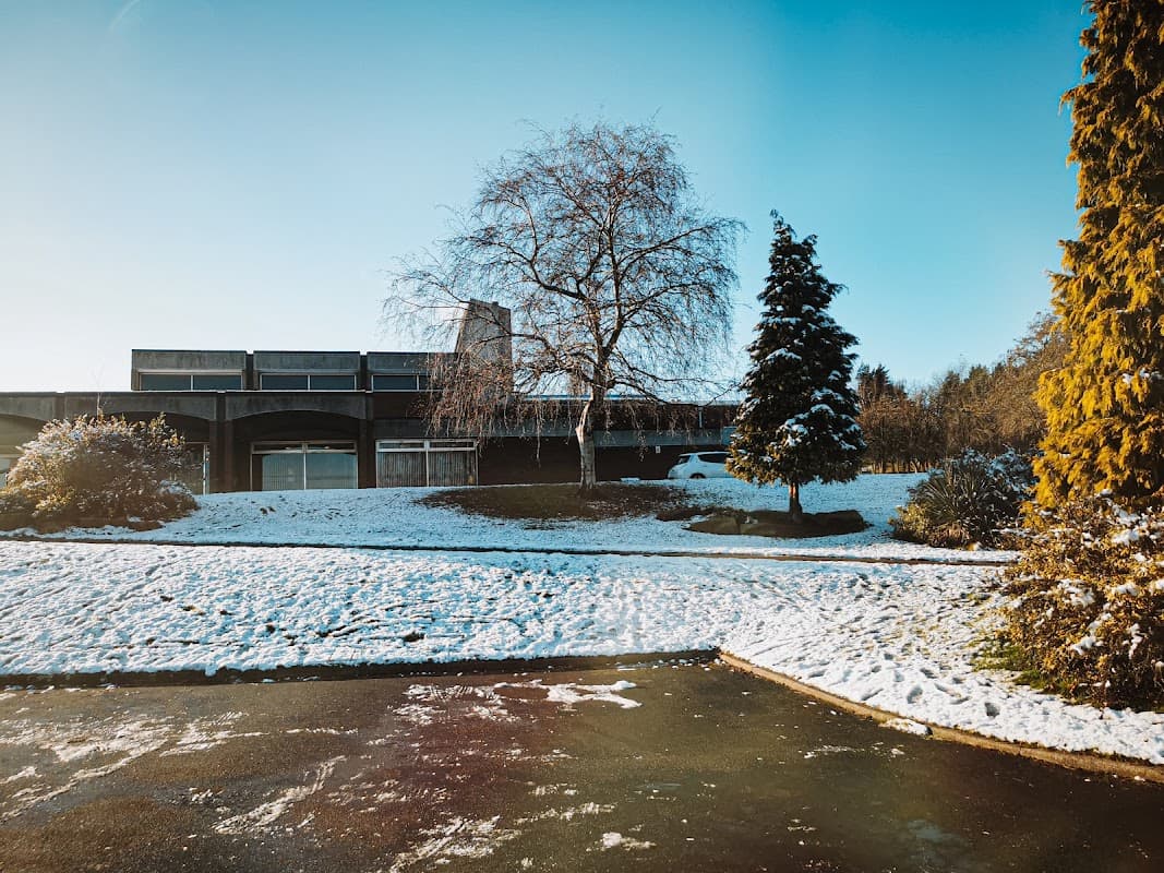 Snow-covered car park at Hutcliffe Wood Crematorium, with a modern building, trees, and clear blue sky.