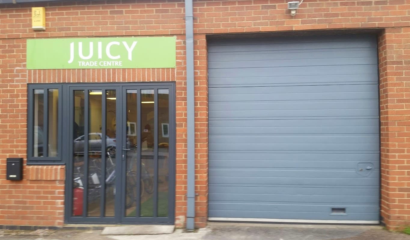 Green brick building with a green sign reading "JUICY TRADE CENTRE" and a gray garage door.