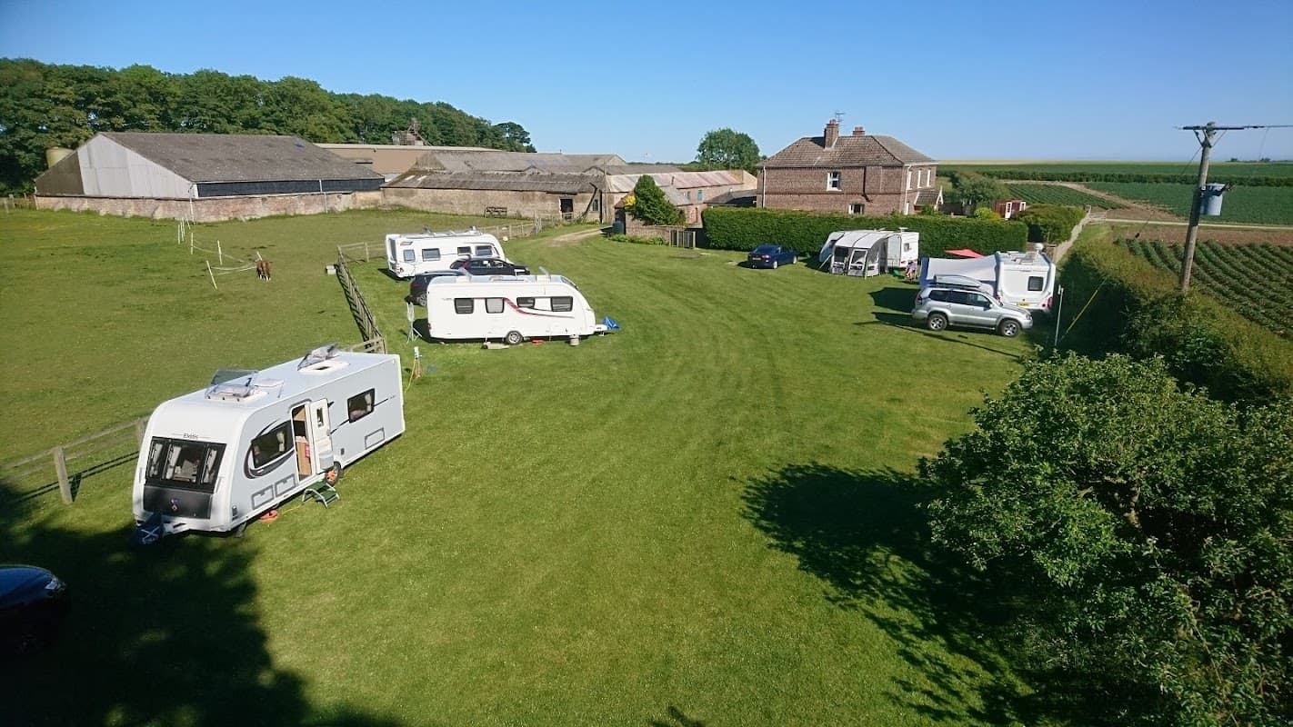Caravans and motorhomes parked on green grass near a farmhouse and fields in sunny Grindale, Yorkshire.