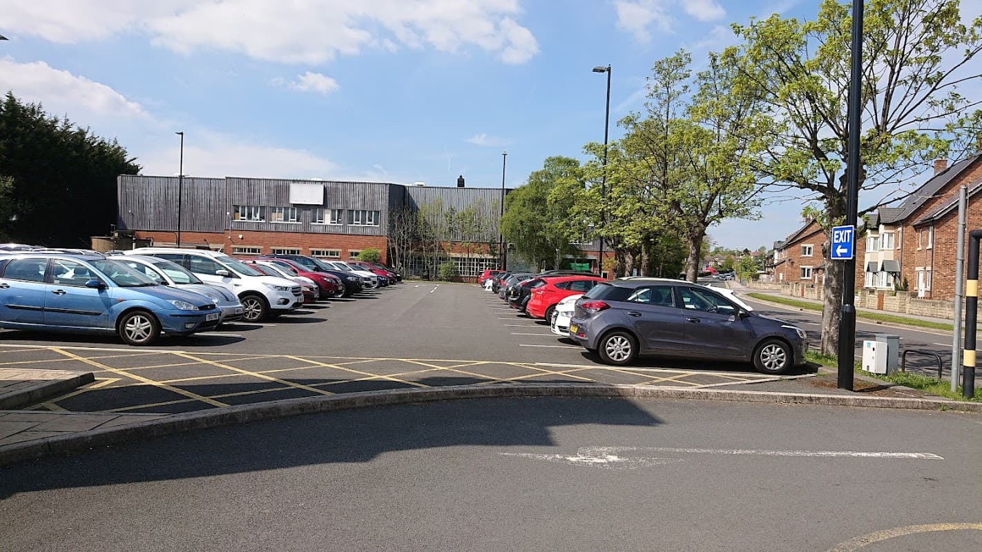 Free parking lot with various parked cars, trees, and a building in the background under a clear blue sky.