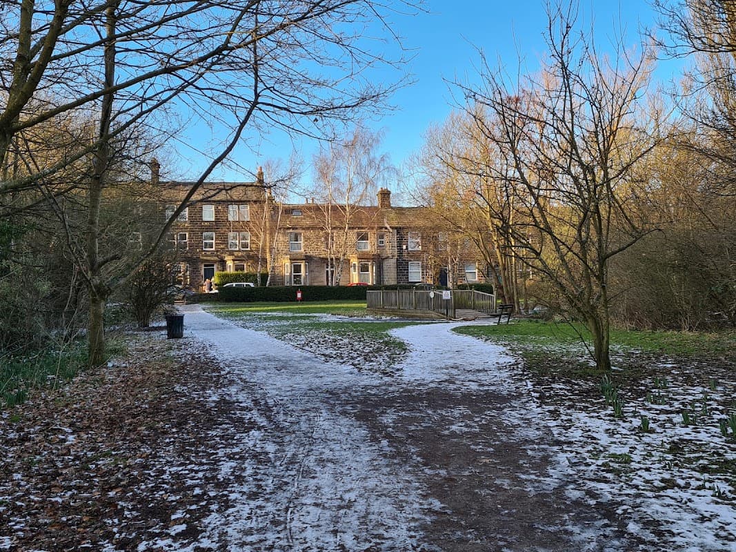 Springfield Park in Guiseley, featuring a path through trees, a grassy area, and historic buildings in the background.