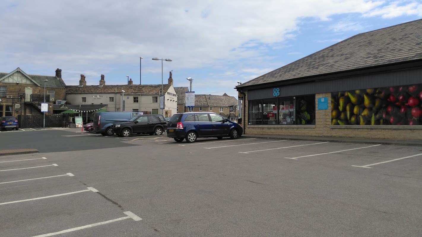 Empty car park with a blue car and a building featuring colorful fruit murals in Guiseley, Yorkshire.