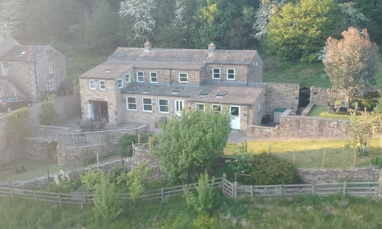 Charming stone cottage surrounded by greenery, featuring a patio and garden in Gunnerside, Yorkshire.