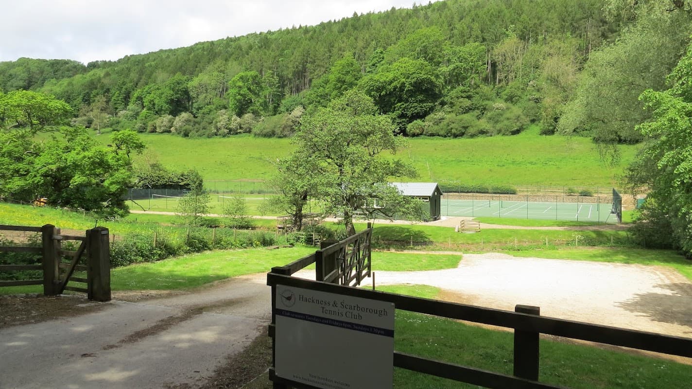 Tennis courts nestled in a lush green valley, framed by trees, with a sign for Hackness and Scarborough Tennis Club.