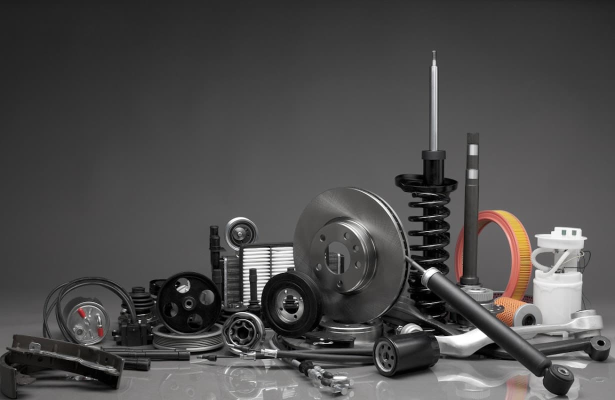 Assorted automotive parts including brake discs, springs, filters, and various mechanical components on a dark background.