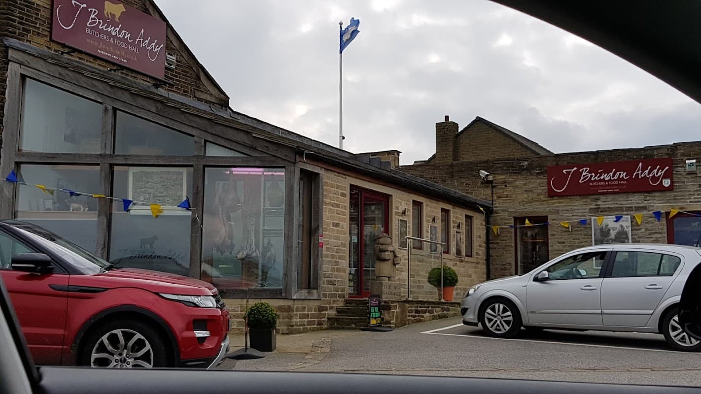 J Brindon Addy Butchers and Food Hall, featuring stone exterior, flags, and parked cars in Hade Edge, Yorkshire.
