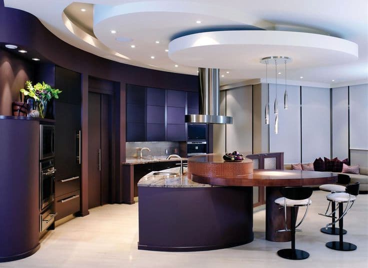 Modern kitchen with curved design, dark cabinetry, sleek appliances, and a central island with bar stools.