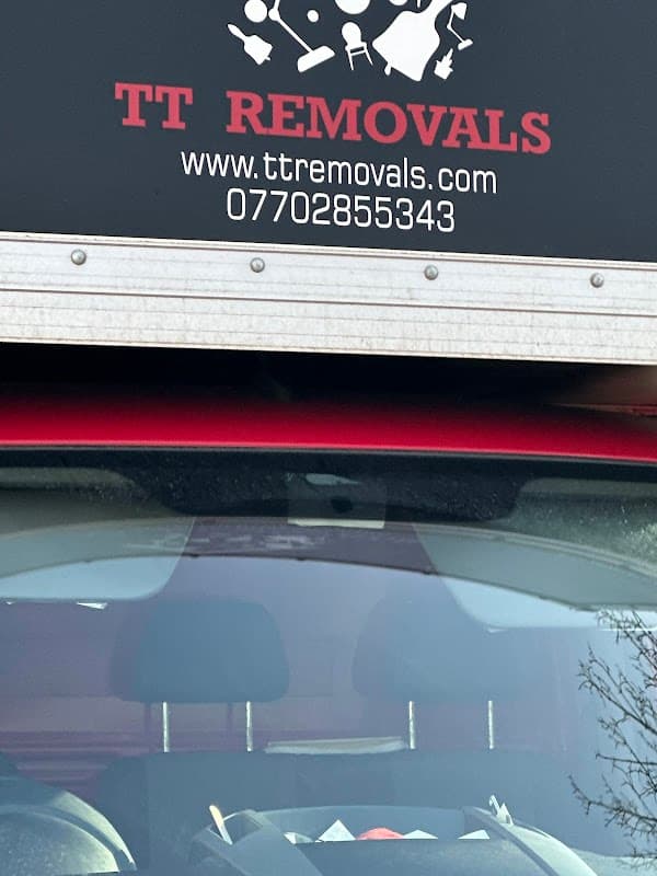 Red van with "TT Removals" sign and contact information, parked in a car park with trees in the background.