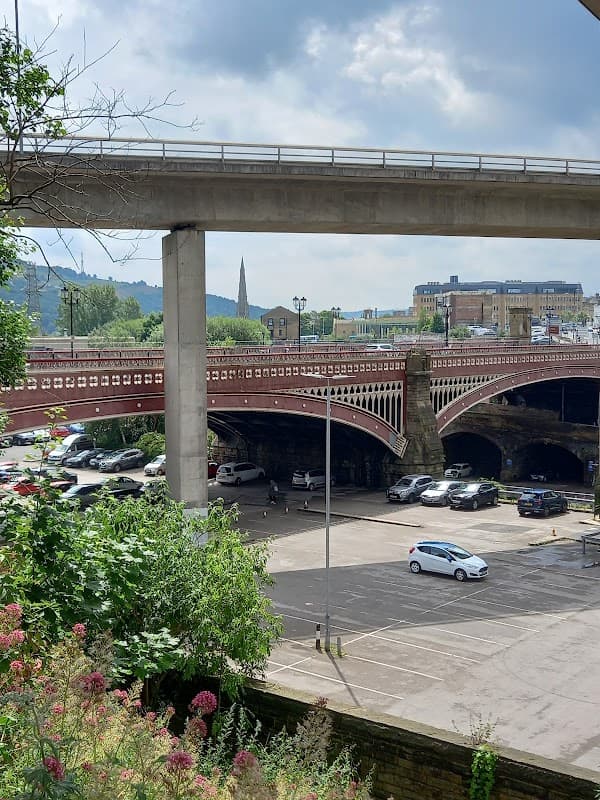 North Bridge Car Park in Halifax, featuring multiple levels, vehicles, and surrounding greenery under a cloudy sky.