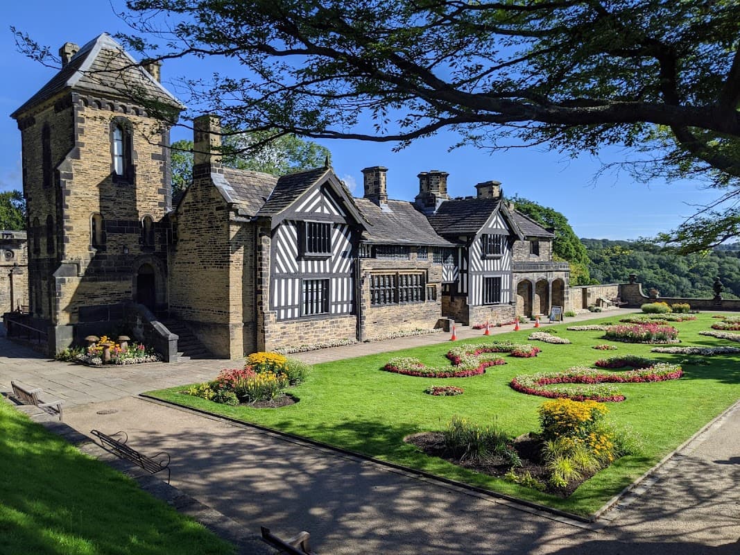 Historic building with black and white timber framing, surrounded by colorful flower gardens and lush greenery.