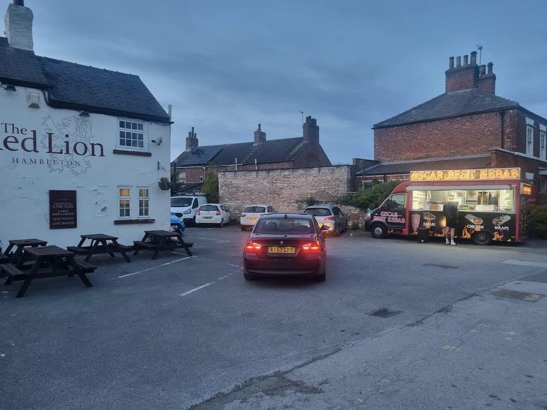 The Red Lion bar with outdoor seating, cars parked, and a food truck in the evening light.