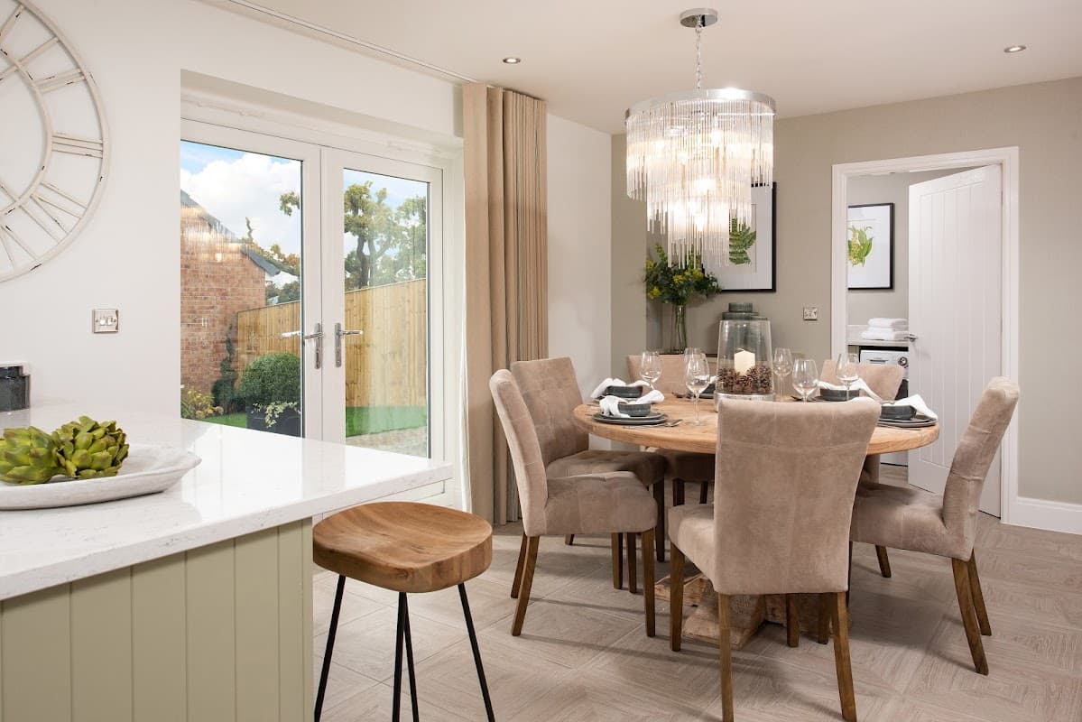 Modern dining area with a round wooden table, plush chairs, a chandelier, and sliding doors leading to a garden.