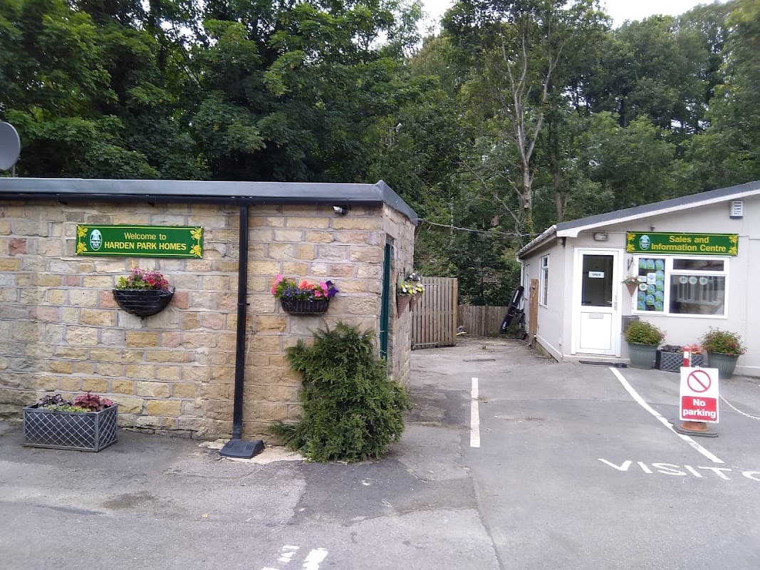 Welcome sign at Harden Park Homes, stone building with flower pots, and an information center with a no parking sign.