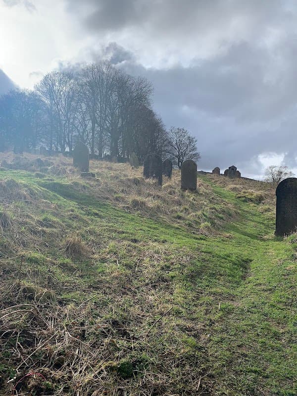 Grassy slope with gravestones, surrounded by trees under a cloudy sky.