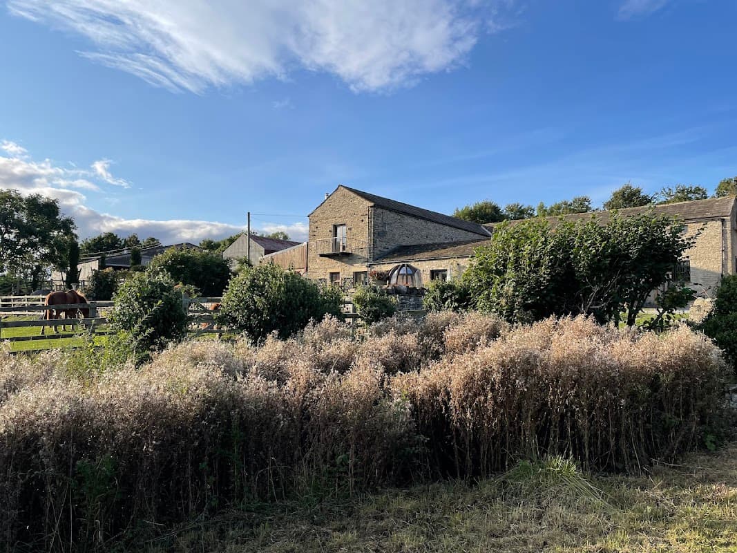 Craken House Farm features stone buildings, lush greenery, horses, and a clear blue sky in Harmby, Yorkshire.
