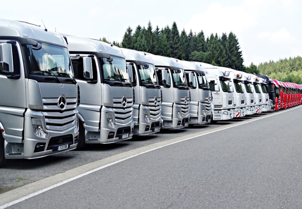 Row of silver trucks parked neatly along a road, surrounded by trees in the background.