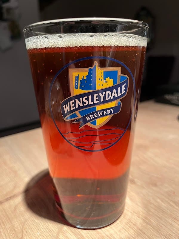 A pint of amber beer in a glass featuring the Wensleydale Brewery logo.