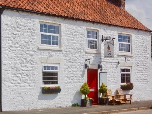 Whitewashed building with a red door, windows with flower boxes, and a sign hanging above the entrance.