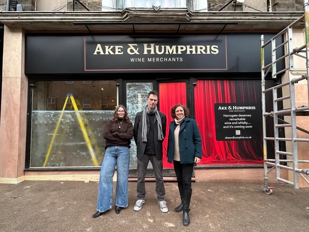 Ake & Humphris Wine Bar & Shop storefront with three people standing in front, scaffolding, and a red curtain backdrop.