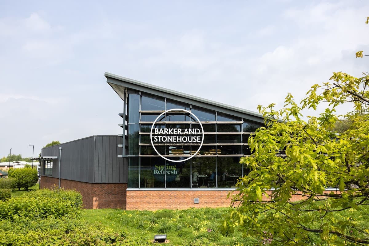 Modern furniture shop with large glass windows, featuring the sign "Barker and Stonehouse" surrounded by greenery.