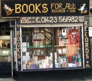 Bookshop window display featuring "Books For All" sign, shelves of books, and contact information.