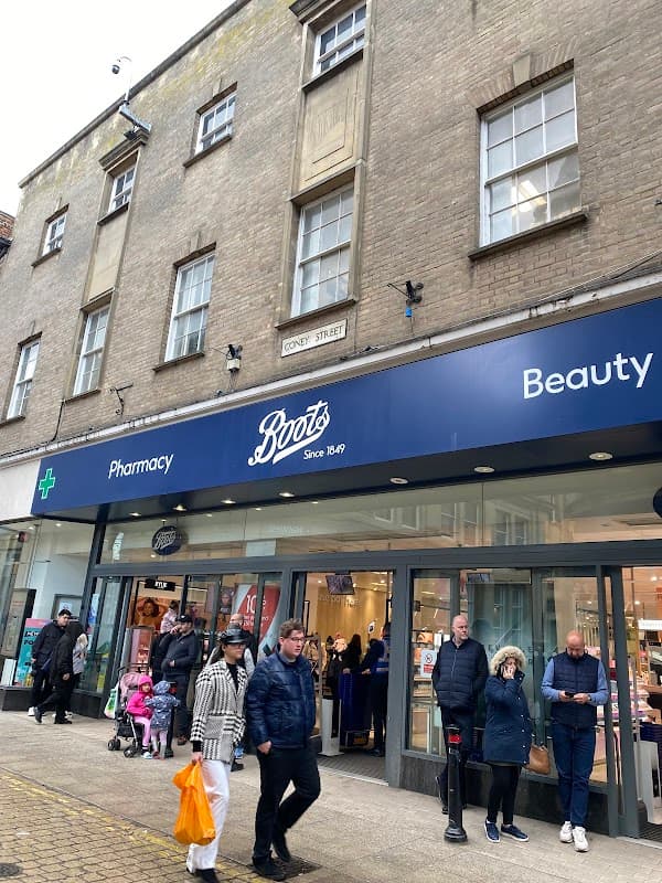 Boots store front featuring "Pharmacy" and "Beauty" signs, with shoppers and a child in a stroller outside.