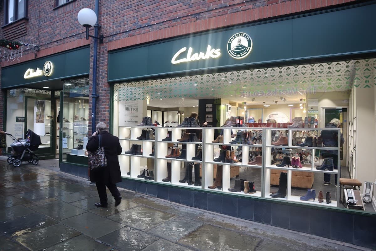 Clarks shoe shop exterior in Harrogate, showcasing a variety of shoes in display windows; rainy pavement visible.