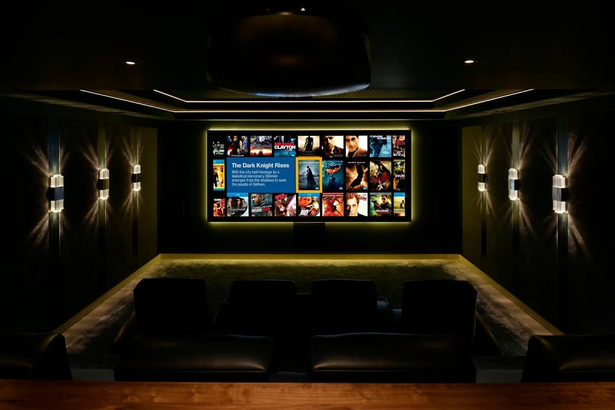 A modern home theater with a large screen displaying movie posters, dark walls, and plush seating.