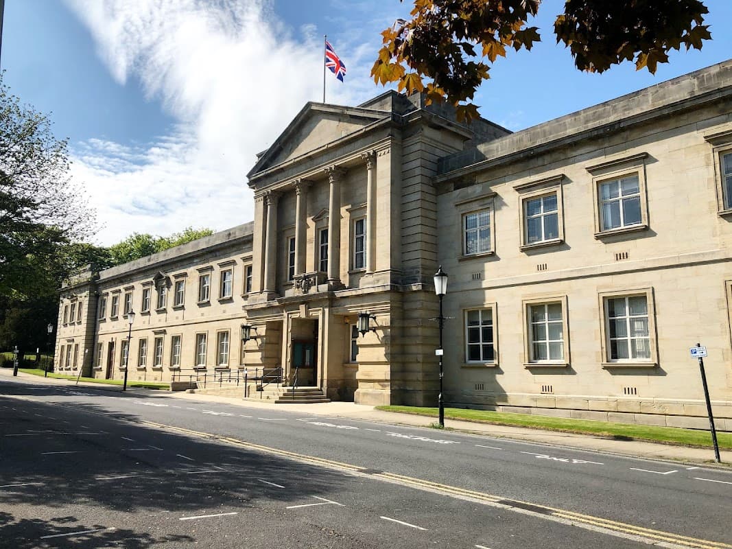 Crescent Gardens in Harrogate features a grand stone building with a flag, surrounded by greenery and a clear blue sky.
