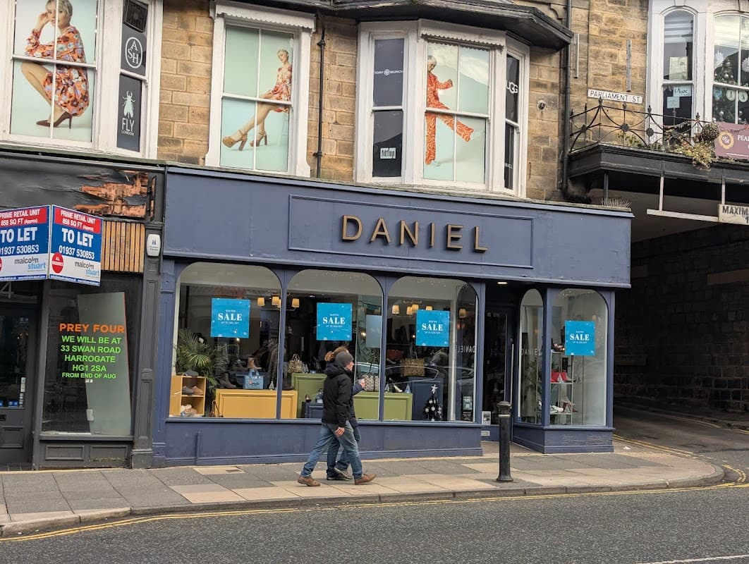 Shoe shop with large windows displaying footwear, sale signs, and a person walking by on a street in Harrogate.