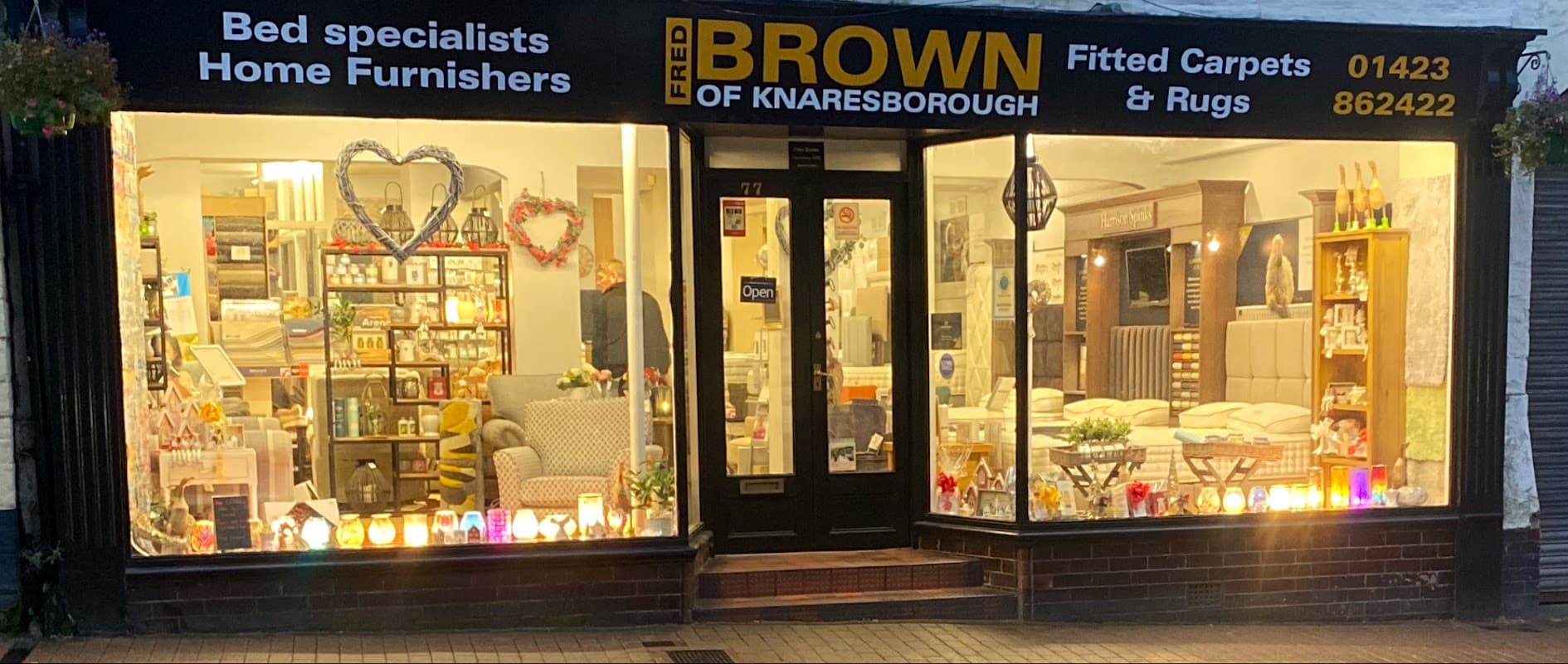 Homeware store with a welcoming display, showcasing beds, carpets, and decorative items, illuminated by soft lighting.